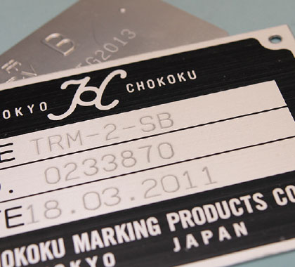 Image of a nameplate engraved with 'TRM-2-SB' for type, '0233870' for number, '18.03.2011' for date, and 'TOKYO CHOKOKU' with logo
