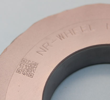 Image of 'NR-WHEEL HR' text and QR code engraved in an arc on a donut-shaped piece of hardened steel